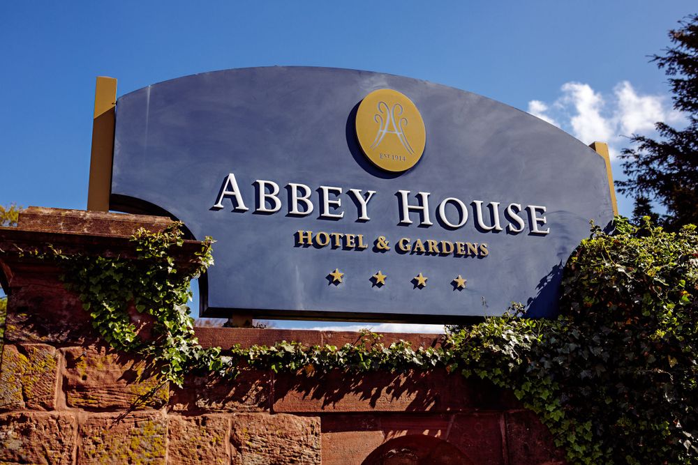 Abbey House Hotel and Gardens signage mounted on stone wall under blue sky.