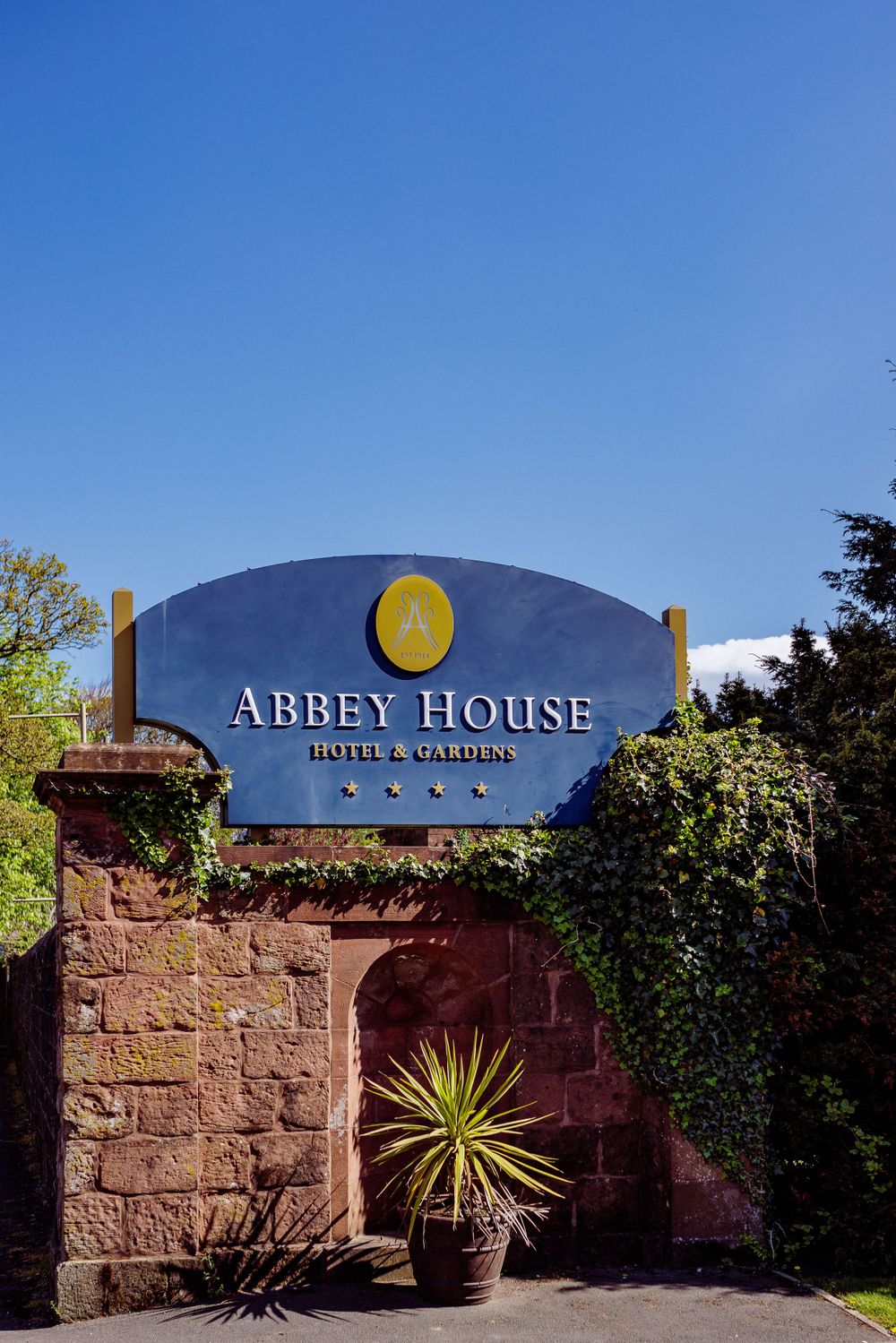 Abbey House hotel entrance sign mounted on red stone wall with ornamental plant.