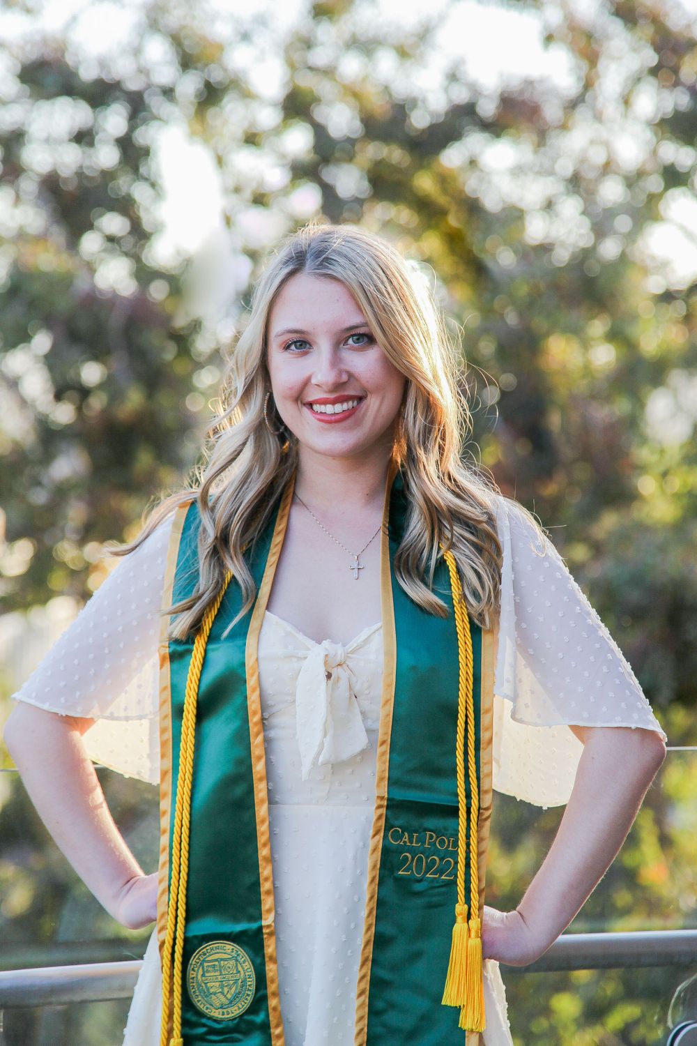 Graduate standing by Cal Poly building with Eucalyptus trees in background.
