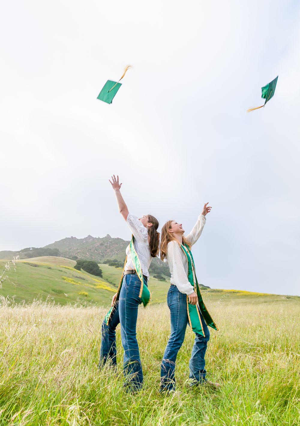 Two graduates tossing caps by Bishop Peak,