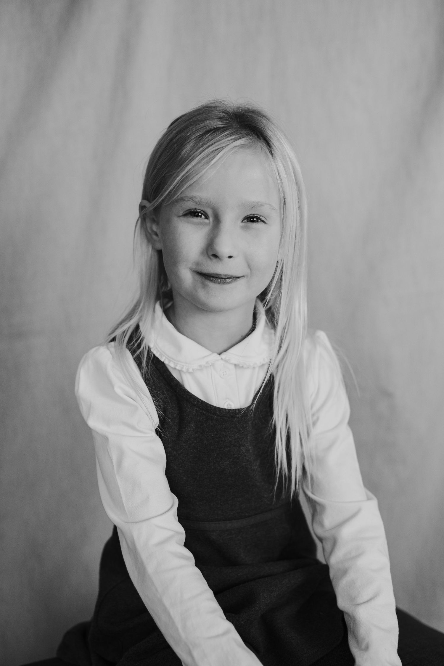 Young student in white blouse and dark pinafore dress poses for school portrait.