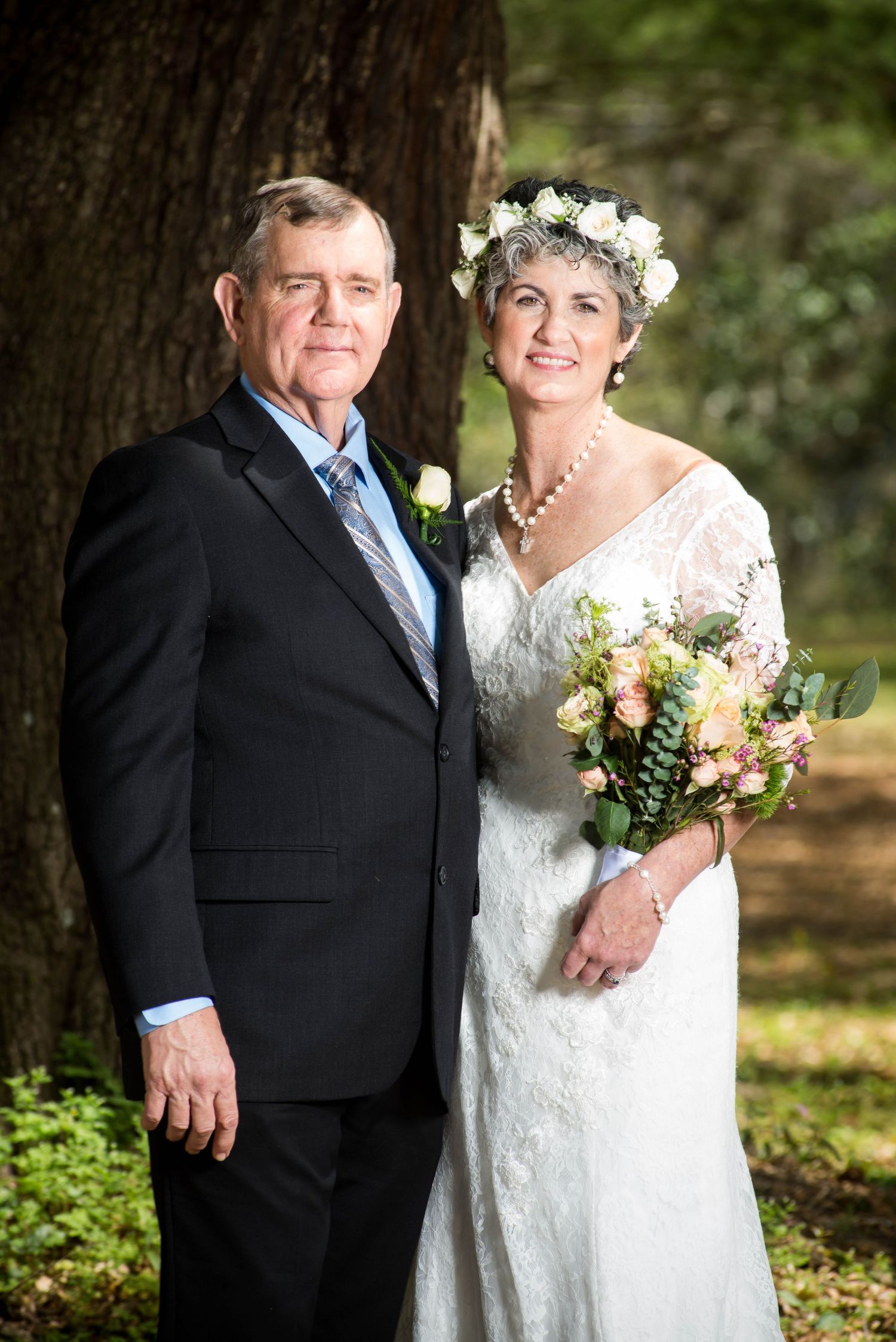 A classic outdoor wedding portrait of a couple standing beneath a tree.