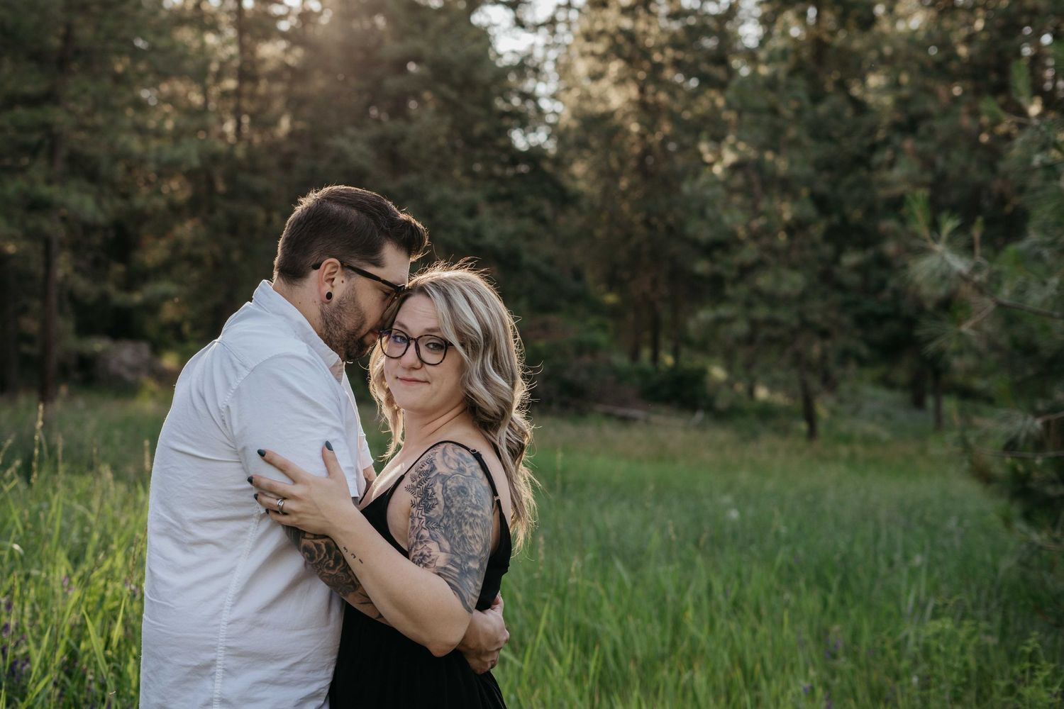Romantic outdoor portrait of couple embracing in sunlit field with forest backdrop.