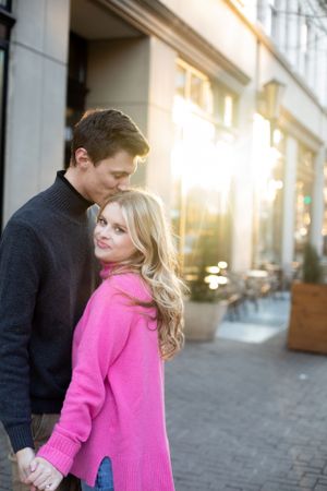 A couple in casual sweaters sharing a tender moment outside a storefront during golden hour.