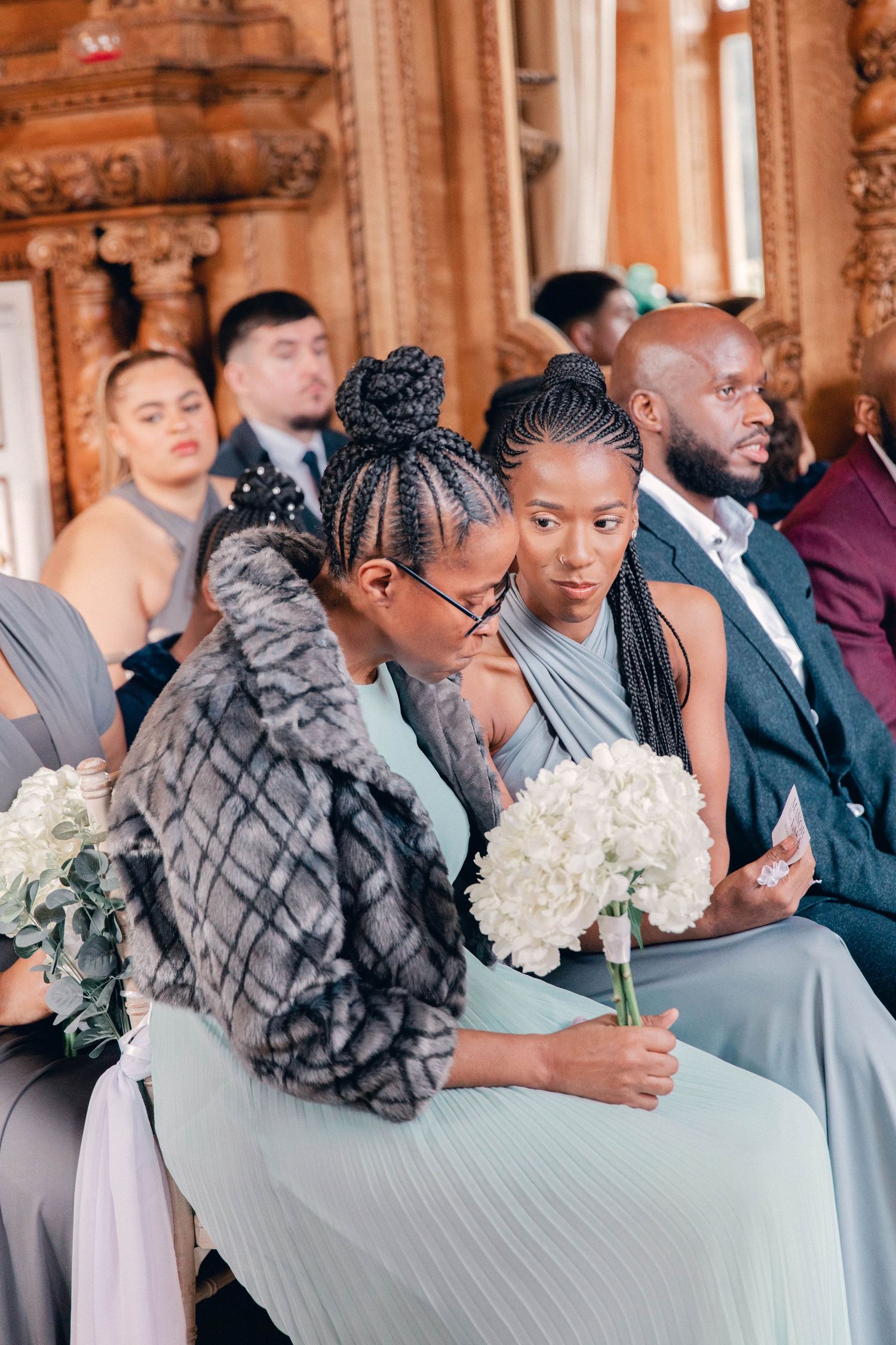 Bridesmaids in light blue dresses hold white bouquets during wedding ceremony in ornate venue.