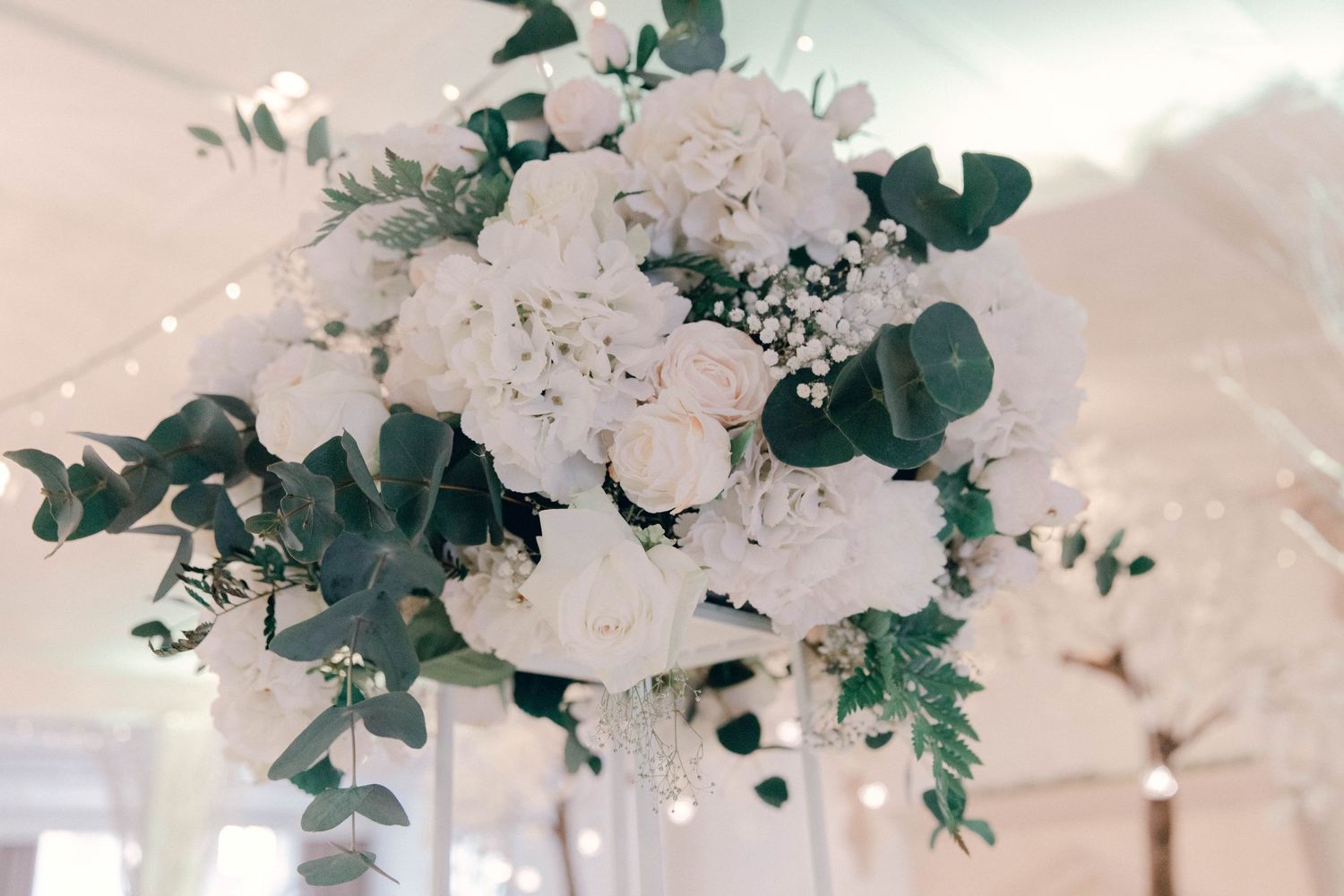 White wedding tables decorated with floral centerpieces and hanging greenery in an ethereal setting.