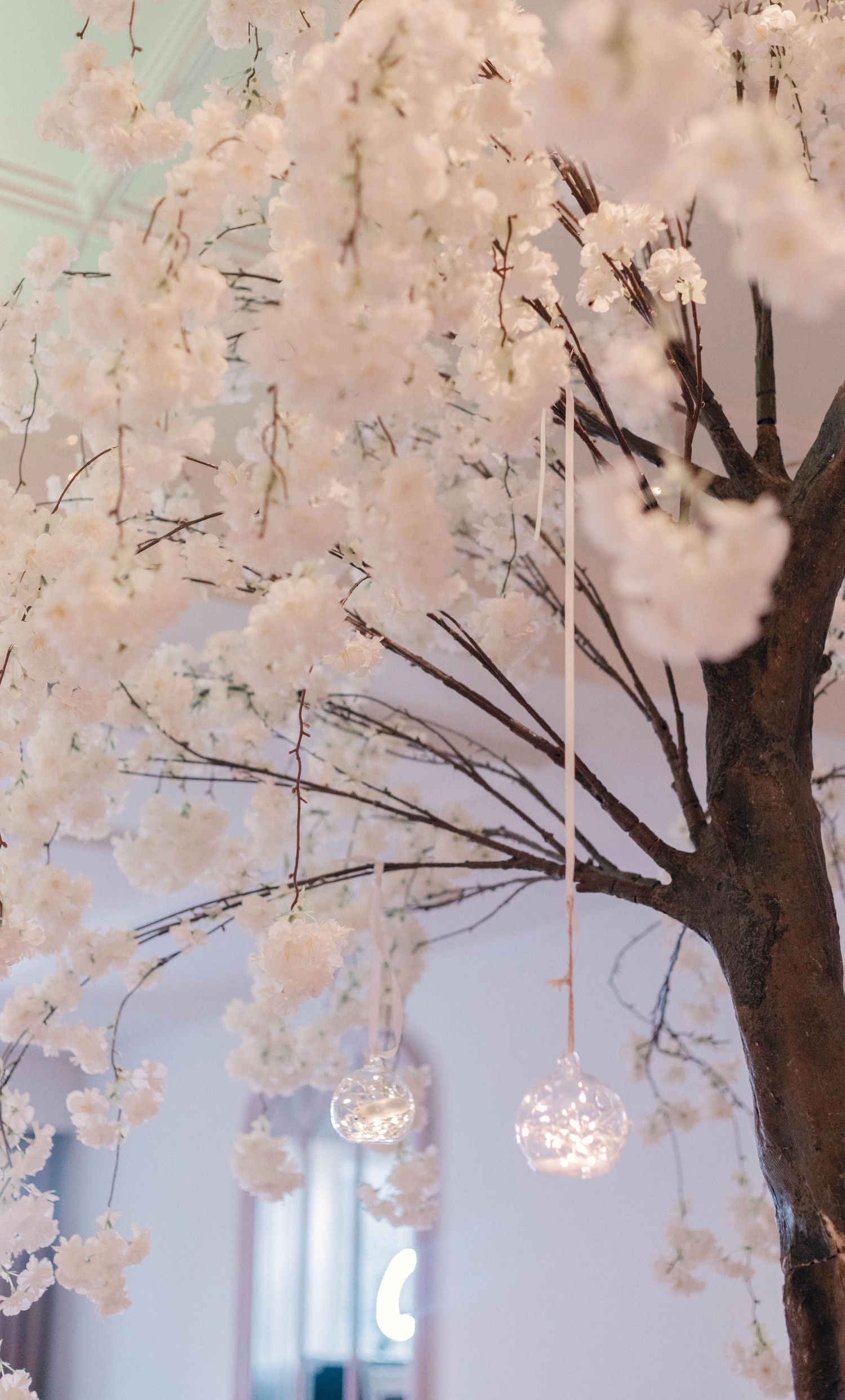 White cherry blossom trees with hanging crystal orbs create a romantic indoor wedding canopy.