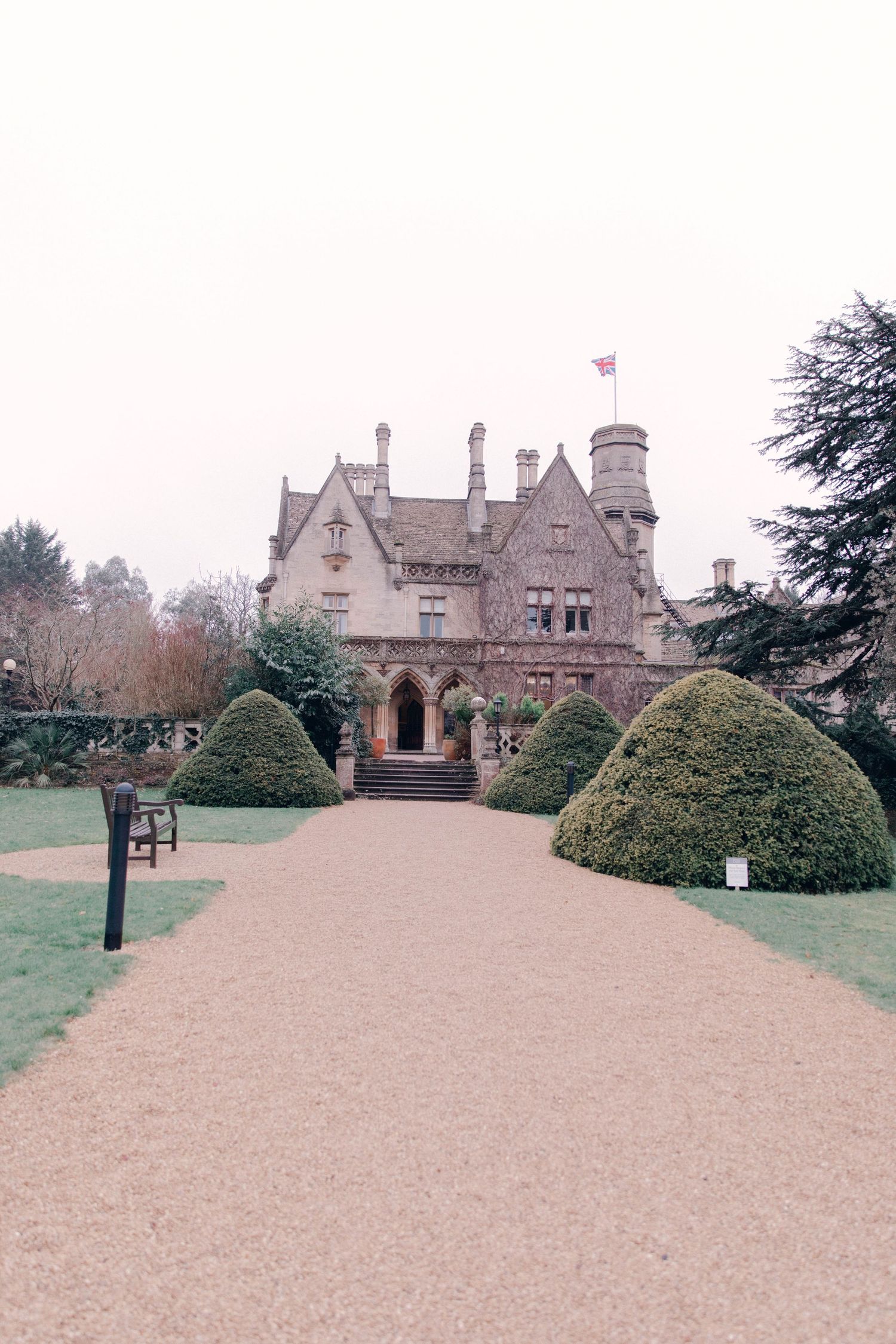Historic Gothic mansion with manicured grounds and stone architecture in foggy weather.