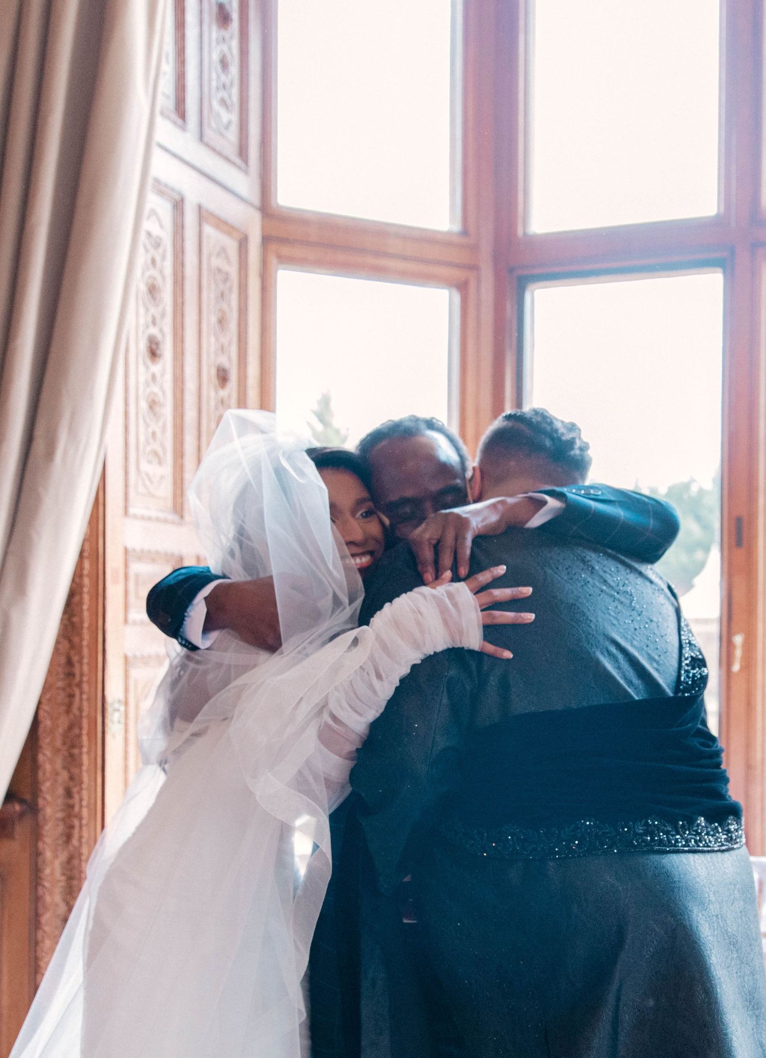 Emotional wedding moment captured in elegant room with bright windows and white curtains.