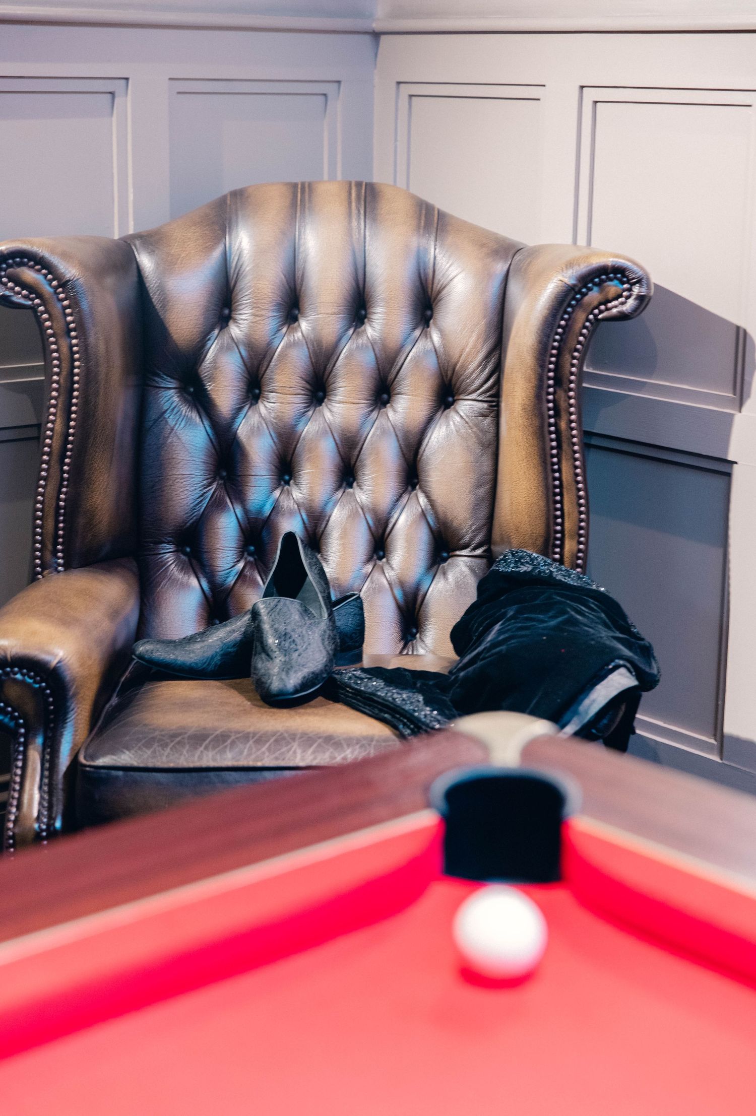 Vintage leather Chesterfield sofa beside a red pool table in an elegant game room.