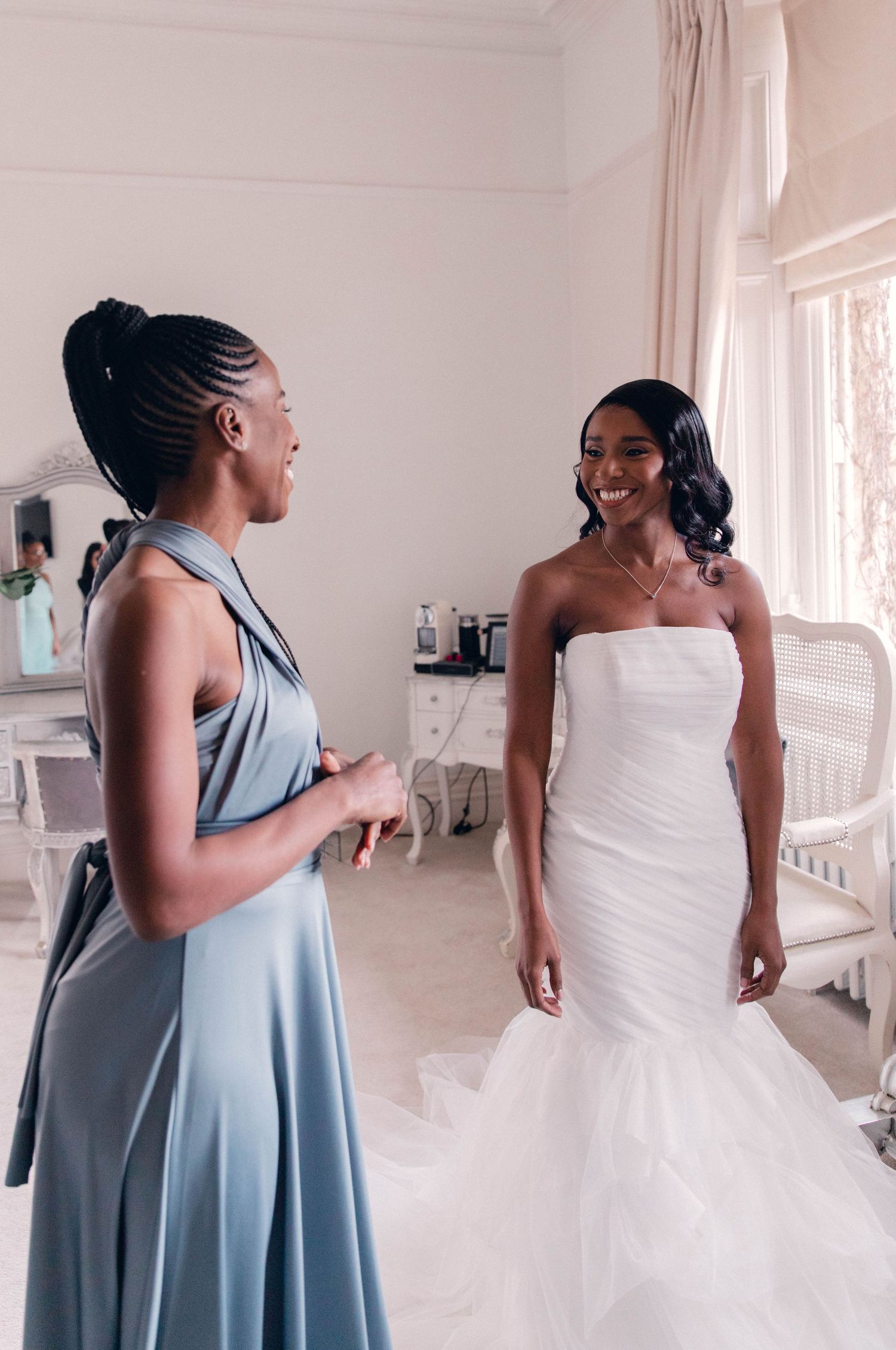 Wedding preparation scene with bride in white gown and bridesmaid in blue dress.