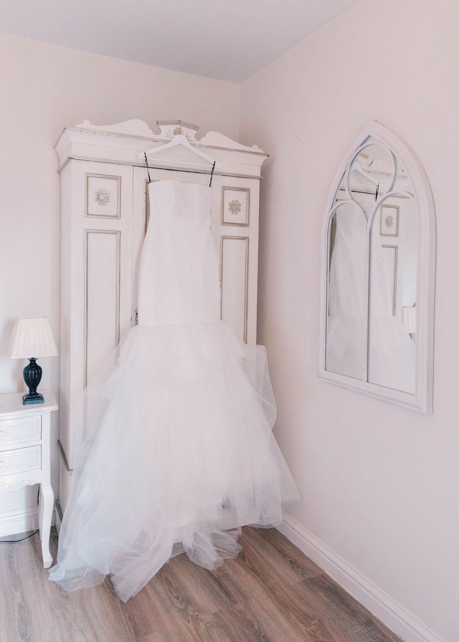White wedding dresses hanging on display in a minimalist dressing room with wooden floors.