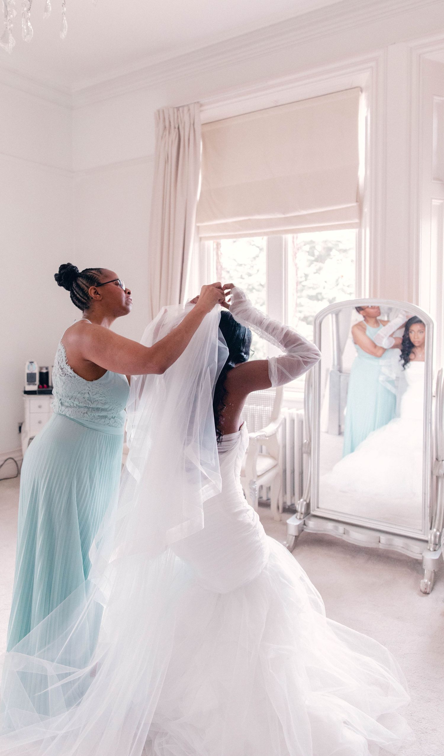 Wedding dress fitting with bridesmaids in light blue dresses helping adjust the gown.
