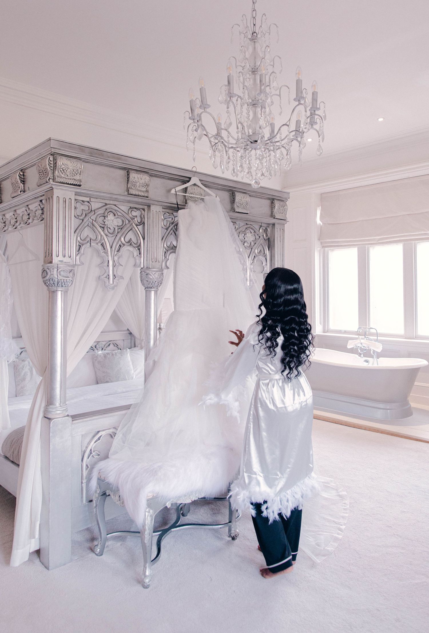 Elegant all-white bedroom with ornate chandelier and canopy bed.