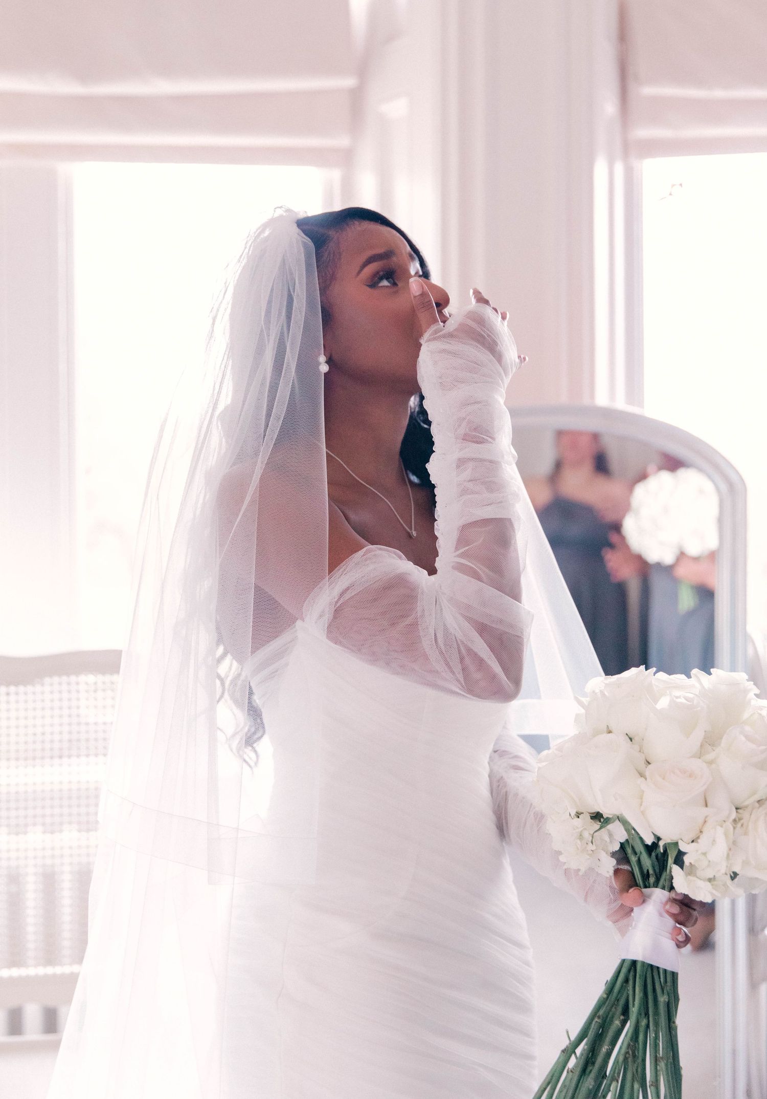 Bride in long-sleeved white dress holding a bouquet of white flowers.