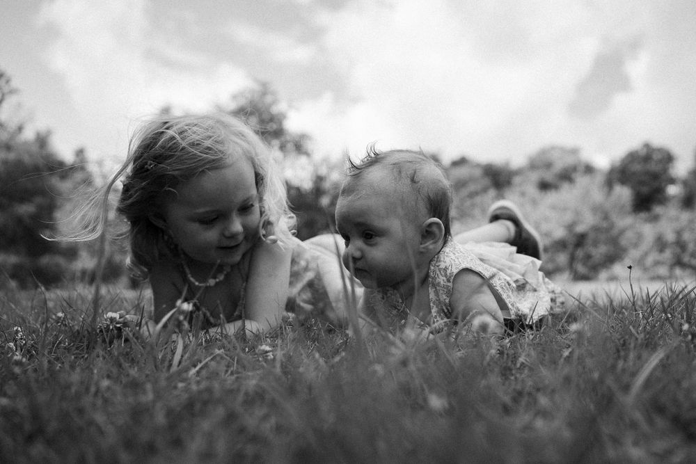 A black and white photo of children lying in grass and flowers sharing a tender moment.