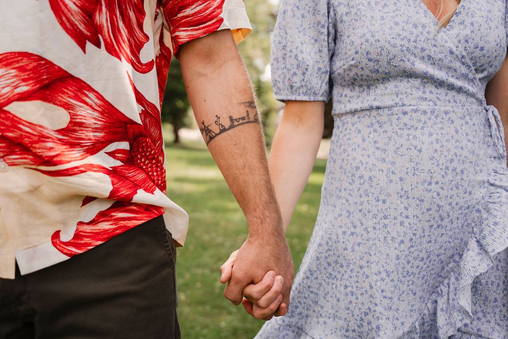 Close-up shot of two people holding hands while wearing red floral and gray clothing.
