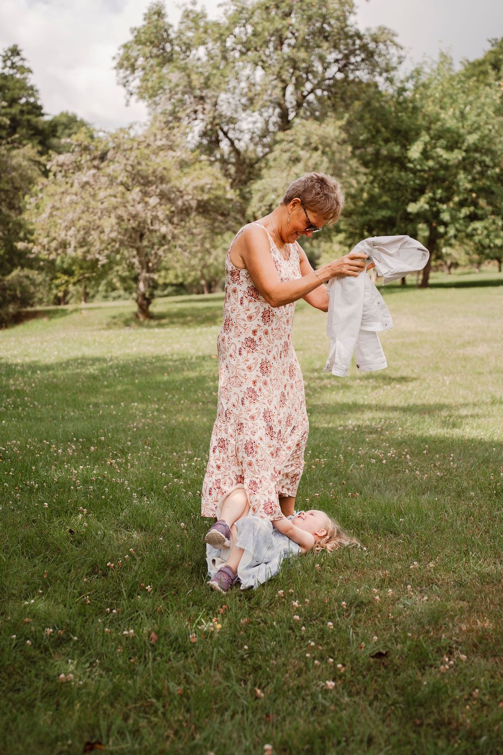 Person in floral dress holding white clothing item while standing in sunny garden setting.