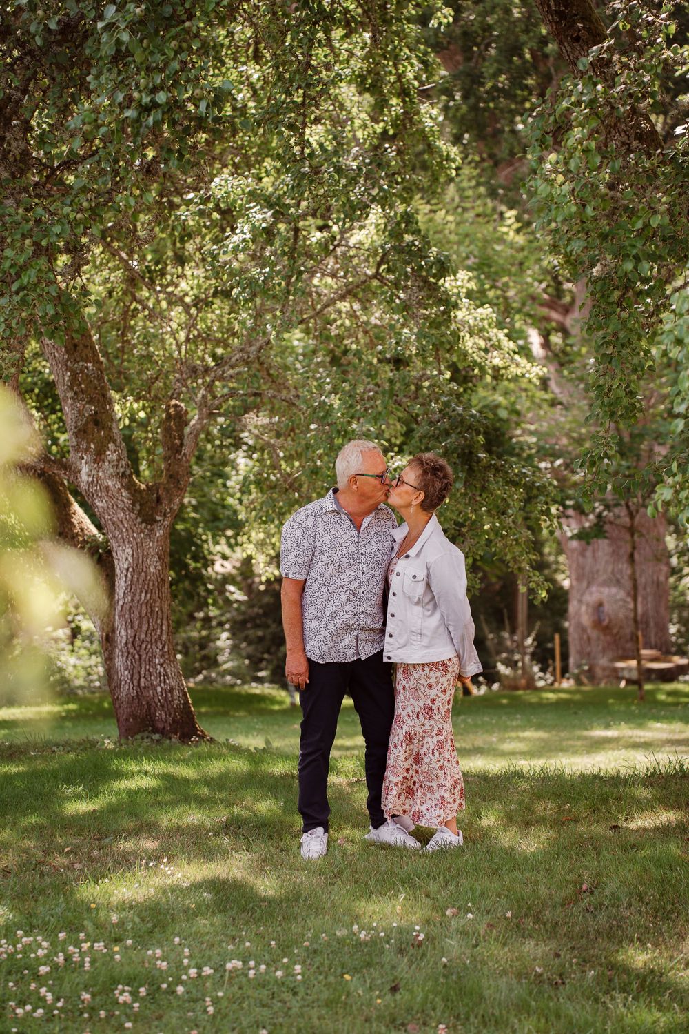 Mature couple sharing an intimate moment under blooming trees in a peaceful garden setting.