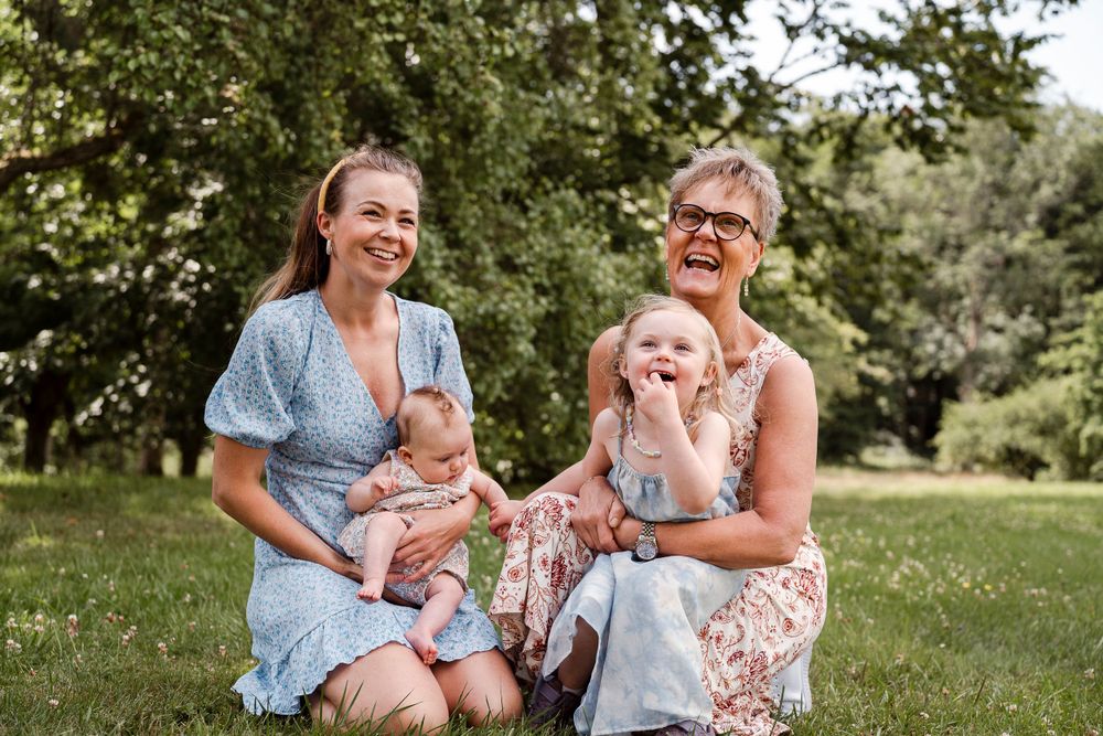 A candid outdoor family moment on grass with adults and babies enjoying a sunny summer day.