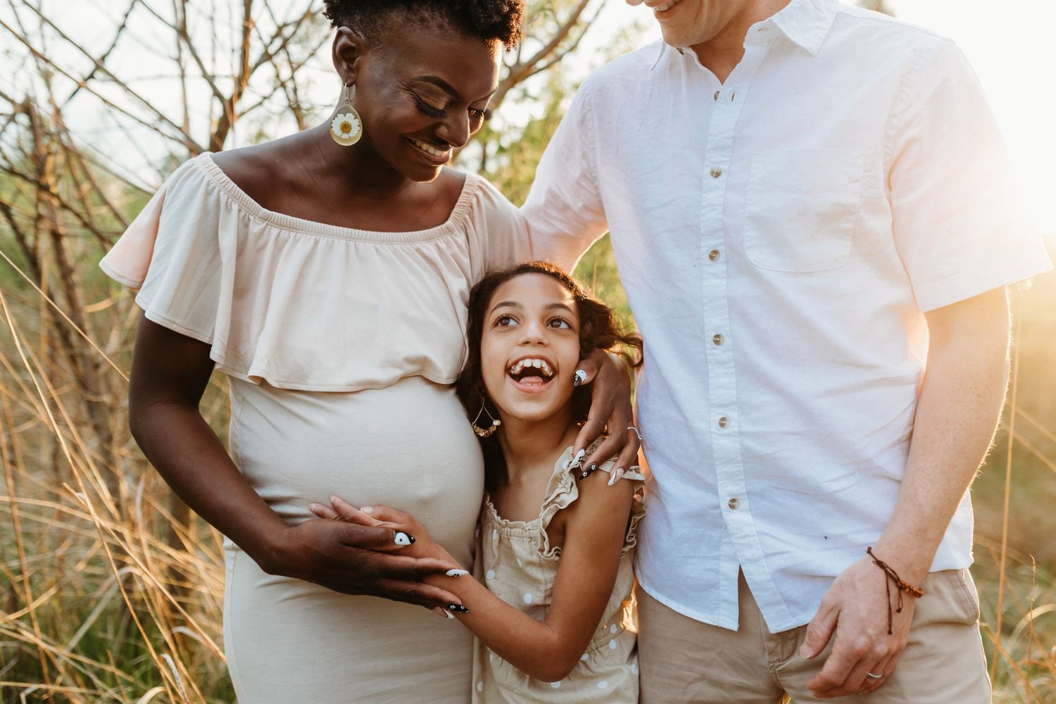 Happy family moment captured in golden sunlight with expectant mother in white dress.