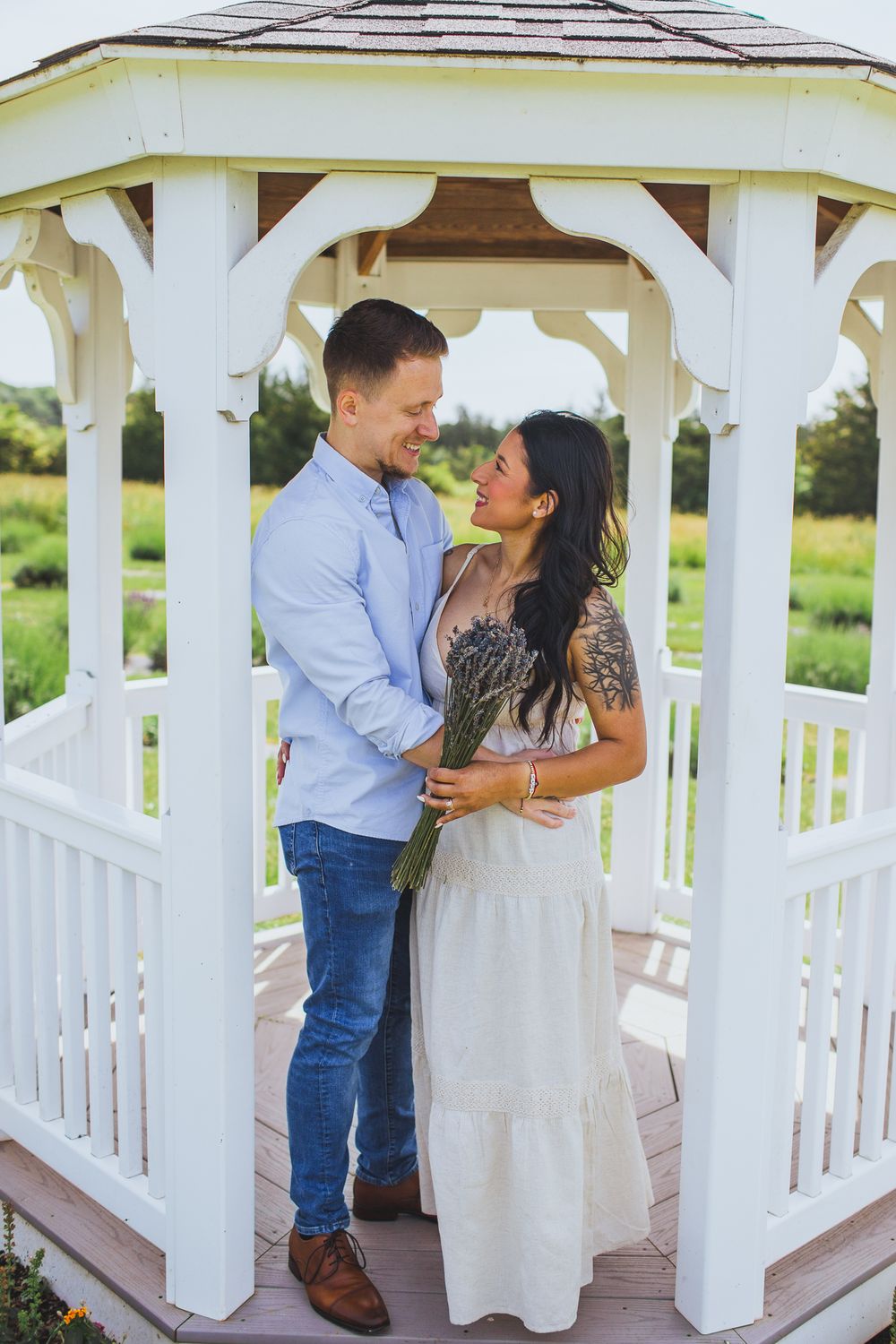A couple shares an intimate moment inside a white wooden gazebo on a sunny day.