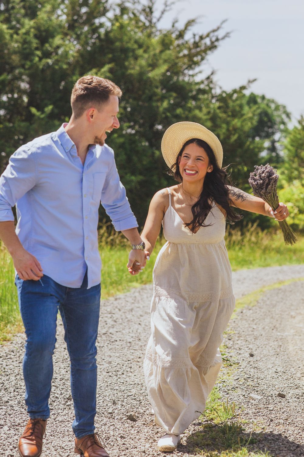 A couple walks joyfully together on a gravel path surrounded by green summer foliage.