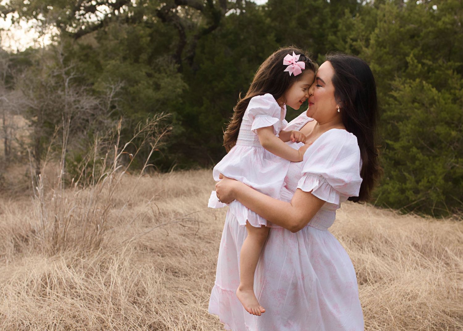Outdoor maternity photography in white dress among tall dried grass at golden hour.