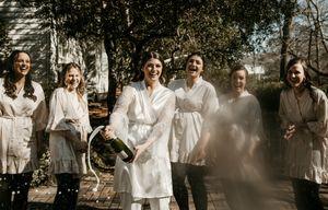 Group photo of wedding party wearing matching cream-colored dresses in sunlight.