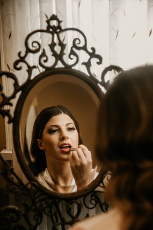 Artistic mirror reflection shows final touches of bridal makeup application.