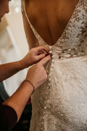 Close-up of hands buttoning an intricate lace wedding dress.