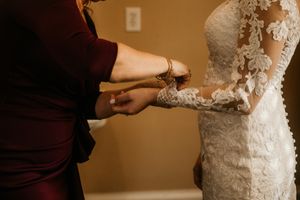 Detailed shot of hands fastening a delicate lace wedding gown.
