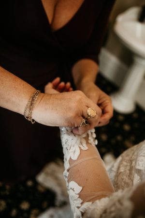 Close-up of hands with jewelry helping with wedding dress preparations.