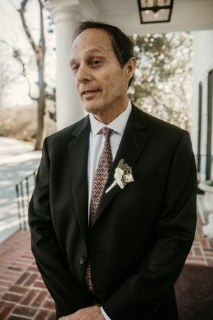 A formal portrait showing wedding attire with a boutonniere against an outdoor backdrop.
