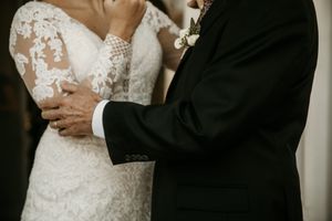 Close-up detail of a wedding couple embracing, showing intricate lace dress details and formal attire.