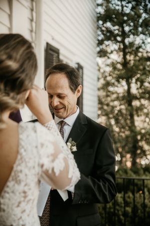 Sweet wedding moment captured on outdoor porch with rustic white siding backdrop.
