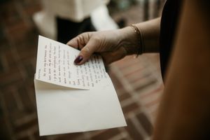 Hand holding handwritten wedding vows against brick background.