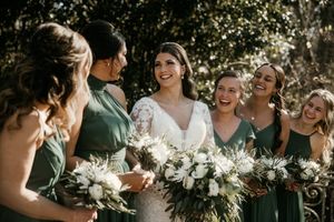 Wedding party with bridesmaids in sage green dresses holding white floral bouquets.