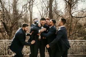 Groomsmen in navy suits laughing and celebrating outdoors with winter trees in background.