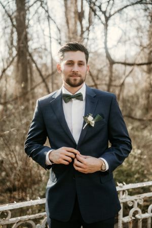 Classic portrait of groom in navy tuxedo and bowtie against winter forest background.