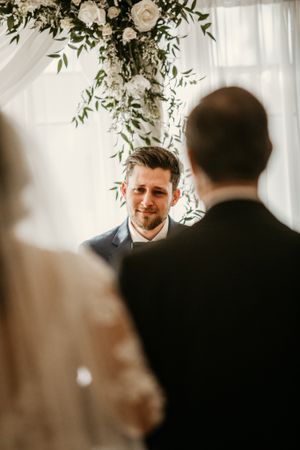 Elegant indoor wedding ceremony with hanging floral decorations and white drapery.