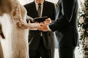 Close-up of couple exchanging rings during wedding ceremony under floral arch.