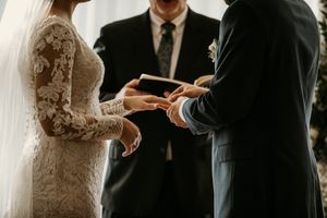 Close-up of couple exchanging rings during wedding ceremony with lace-sleeved bridal gown.