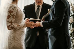 Close-up shot of wedding ring exchange with bride in lace sleeves and groom in black suit.