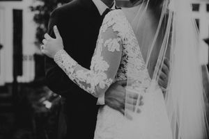 Black and white detail shot of bride's lace sleeve and veil against groom's suit.