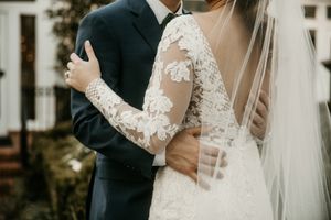 Close-up view of intricate lace sleeves on wedding dress as couple embraces.
