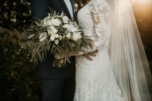 Detail shot of elegant white wedding bouquet against lace dress and dark suit.