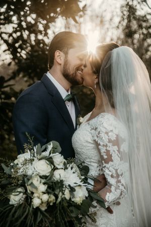 Sunlit wedding portrait with white floral bouquet against natural forest backdrop.