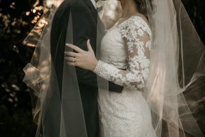 A close-up of a couple embracing in wedding attire with delicate lace details and flowing veil in natural lighting.