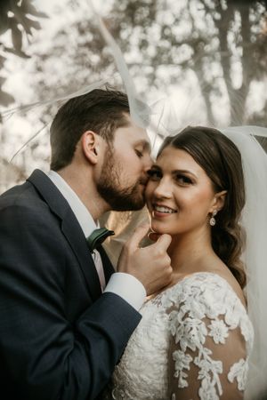Intimate wedding portrait showing a tender moment between newlyweds with sunlit forest in background.